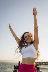 Happy woman with arms raised in front of sky - DCRF01912