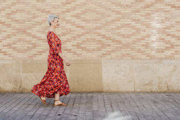 Lächelnde Frau in rotem Kleid geht vor einer Mauer - JCZF01270