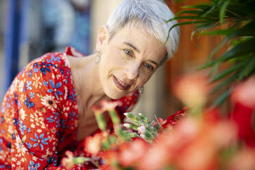 Smiling woman wearing red dress staring at flowers - JCZF01283