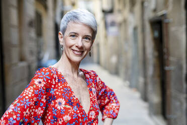 Smiling woman wearing red dress standing in alley - JCZF01286