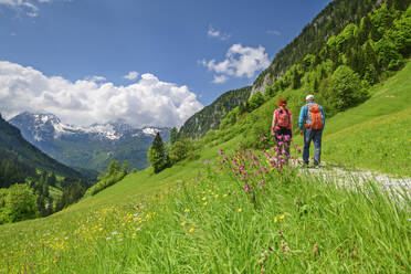 Mann und Frau wandern mit Rucksäcken vor den Berchtesgadener Alpen an einem sonnigen Tag - ANSF00641