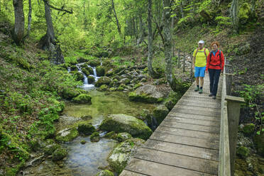 Smiling mature woman walking with man on wooden footbridge in forest - ANSF00648