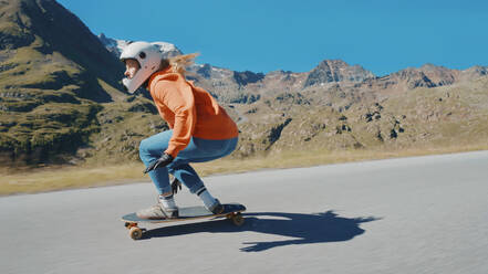 Cinematic downhill longboard session. Young woman skateboarding and making tricks between the curves on a mountain pass. Concept about extreme sports and people - DMDF04479