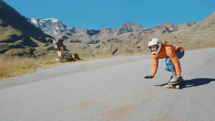 Cinematic downhill longboard session. Young woman skateboarding and making tricks between the curves on a mountain pass. Concept about extreme sports and people - DMDF04480