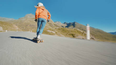 Cinematic downhill longboard session. Young woman skateboarding and making tricks between the curves on a mountain pass. Concept about extreme sports and people - DMDF04483