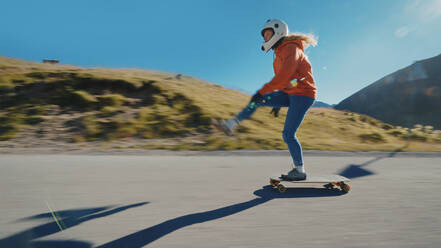 Cinematic downhill longboard session. Young woman skateboarding and making tricks between the curves on a mountain pass. Concept about extreme sports and people - DMDF04485