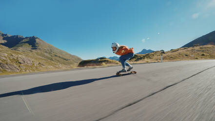 Cinematic downhill longboard session. Young woman skateboarding and making tricks between the curves on a mountain pass. Concept about extreme sports and people - DMDF04486