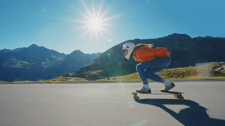 Cinematic downhill longboard session. Young woman skateboarding and making tricks between the curves on a mountain pass. Concept about extreme sports and people - DMDF04491