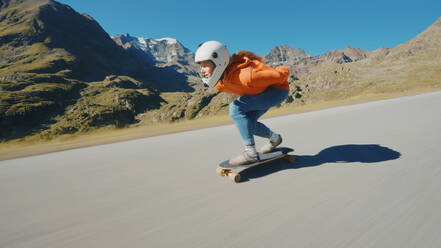 Cinematic downhill longboard session. Young woman skateboarding and making tricks between the curves on a mountain pass. Concept about extreme sports and people - DMDF04494