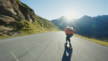 Cinematic downhill longboard session. Young woman skateboarding and making tricks between the curves on a mountain pass. Concept about extreme sports and people - DMDF04497