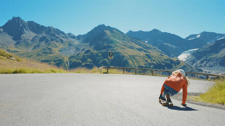 Cinematic downhill longboard session. Young woman skateboarding and making tricks between the curves on a mountain pass. Concept about extreme sports and people - DMDF04505