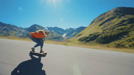 Cinematic downhill longboard session. Young woman skateboarding and making tricks between the curves on a mountain pass. Concept about extreme sports and people - DMDF04506