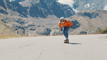 Cinematic downhill longboard session. Young woman skateboarding and making tricks between the curves on a mountain pass. Concept about extreme sports and people - DMDF04507