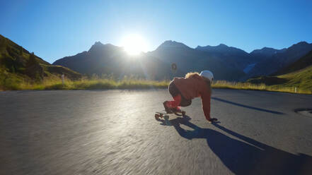 Cinematic downhill longboard session. Young woman skateboarding and making tricks between the curves on a mountain pass. Concept about extreme sports and people - DMDF04509