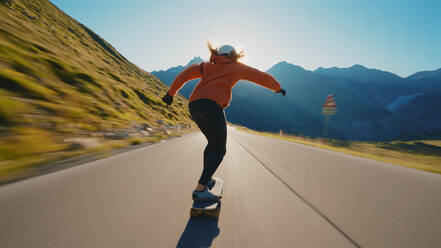 Cinematic downhill longboard session. Young woman skateboarding and making tricks between the curves on a mountain pass. Concept about extreme sports and people - DMDF04510