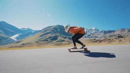 Cinematic downhill longboard session. Young woman skateboarding and making tricks between the curves on a mountain pass. Concept about extreme sports and people - DMDF04513