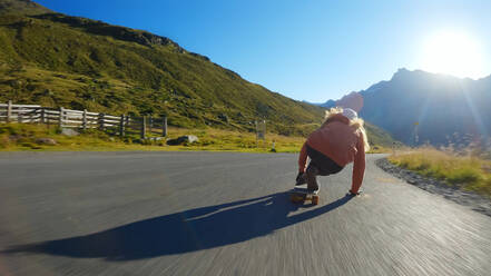 Cinematic downhill longboard session. Young woman skateboarding and making tricks between the curves on a mountain pass. Concept about extreme sports and people - DMDF04515