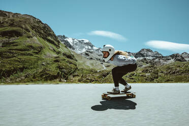 Cinematic downhill longboard session. Young woman skateboarding and making tricks between the curves on a mountain pass. Concept about extreme sports and people - DMDF04519