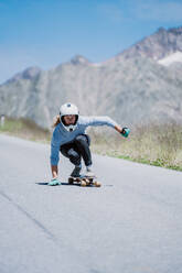 Cinematic downhill longboard session. Young woman skateboarding and making tricks between the curves on a mountain pass. Concept about extreme sports and people - DMDF04520