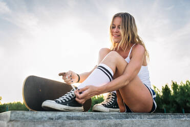 Stylish young woman skating outdoors - Pretty female skater playing with her skate - DMDF04704