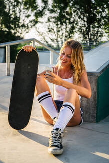 Stylish young woman skating outdoors - Pretty female skater playing with her skate - DMDF04706