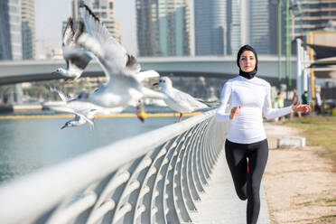 Arabic woman running outdoor and wearing hijab - DMDF04718