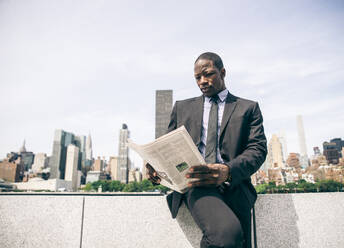 Confident businessman. Successful young man in full suit reading financial news on newspaper and drinking a cup of coffee - DMDF04824