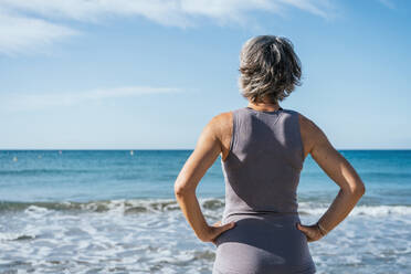 Frau mit Händen auf der Hüfte vor einem Strand stehend - GDBF00076