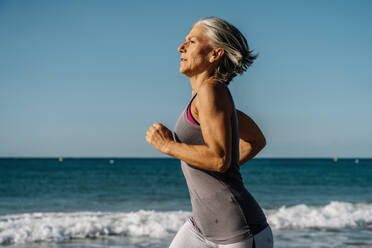 Ältere Frau joggt in der Nähe des Meeres am Strand - GDBF00078