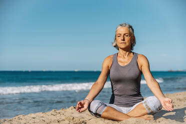Ältere Frau sitzt mit gekreuzten Beinen und meditiert am Strand - GDBF00082