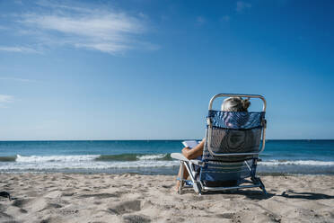 Frau sitzt auf einem Liegestuhl und liest ein Buch am Strand - GDBF00085