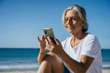 Lächelnde Frau mit Smartphone am Strand - GDBF00090