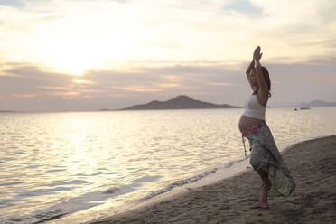 Pregnant woman doing yoga at beach - DMHF00151