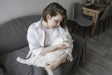 Junge Frau streichelt Katze auf Sofa - YBF00202