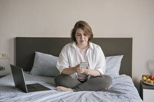 Young freelancer using smart phone on bed at home - YBF00207