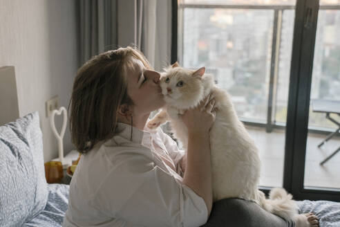 Junge Frau küsst Katze auf Bett zu Hause - YBF00211