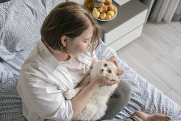 Glückliche Frau spielt mit Katze auf Bett zu Hause - YBF00212