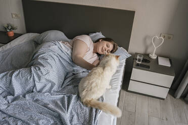 Happy woman relaxing with cat on bed at home - YBF00213