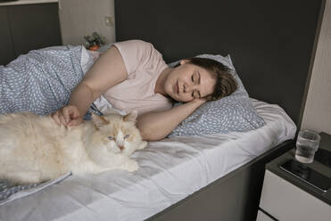 Junge Frau schläft neben der Katze auf dem Bett zu Hause - YBF00214