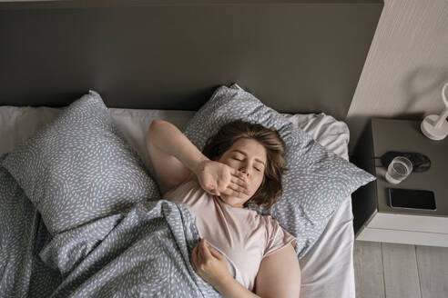 Junge Frau gähnt auf dem Bett zu Hause - YBF00217