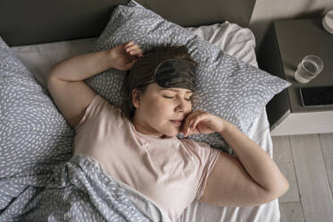 Junge Frau mit Augenmaske schläft auf dem Bett zu Hause - YBF00218