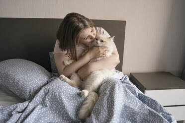 Woman kissing and stroking cat on bed at home - YBF00225