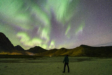 Photographer contemplating the Aurora Borealis (Northern Lights) in the starry sky from Haukland beach, Lofoten Islands, Nordland, Norway, Scandinavia, Europe - RHPLF27360