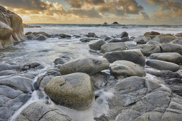 Atlantic rollers surge around shoreline granite boulders on a rising tide at sunset, Porth Nanven, a remote cove near St. Just, in the far west of Cornwall, England, United Kingdom, Europe - RHPLF27923