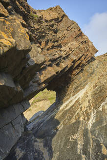 A sunlit view of a rock arch, formed from multiple layers of red sedimentary rock, at Hartland Quay, on the Atlantic coast of Devon, England, United Kingdom, Europe - RHPLF27930