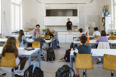 Male and female teacher teaching students sitting on bench in classroom - MASF38295