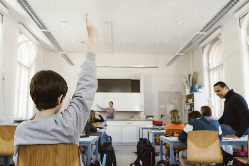 Rear view of schoolboy raising hand while attending lecture in classroom - MASF38297