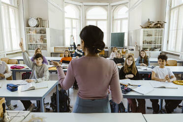 Rear view of female teacher asking students while teaching in classroom - MASF38299