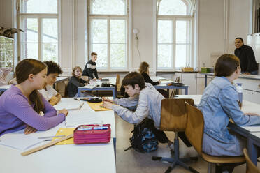 Schoolboy assisting friends sitting on desk in classroom - MASF38308