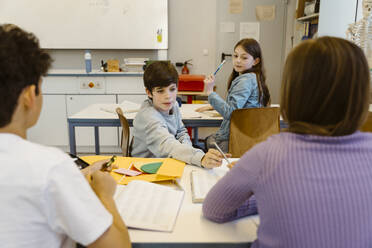 Boy taking pencil from female friend sitting at desk in classroom - MASF38318
